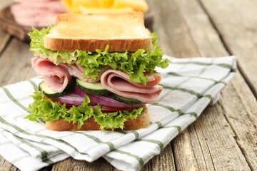 Tasty sandwich with ham and vegetables on wooden table, closeup. Space for text