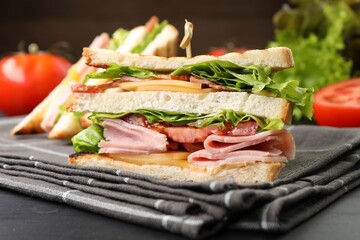 Tasty sandwiches with ham, bacon, cheese and vegetables on black wooden table, closeup