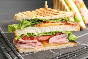 Tasty sandwiches with ham, bacon, cheese and vegetables on table, closeup