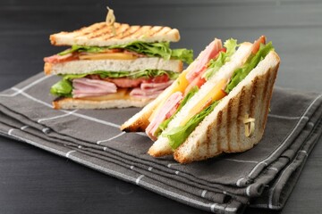 Tasty sandwiches with ham, bacon, cheese and vegetables on black wooden table, closeup