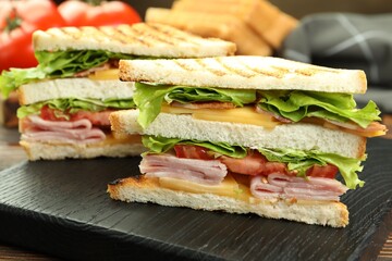 Tasty sandwiches with ham, bacon, cheese and vegetables on wooden table, closeup