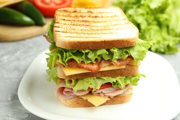 Tasty sandwich with ham, bacon, cheese and vegetables on grey textured table, closeup