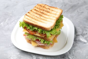 Tasty sandwich with ham, bacon, cheese and vegetables on grey textured table, closeup