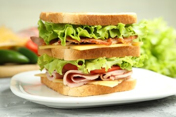 Tasty sandwich with ham, bacon, cheese and vegetables on grey textured table, closeup