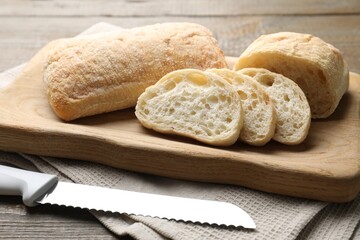 Fresh crispy ciabattas and knife on wooden table, closeup