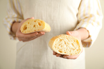 Woman holding halves of fresh ciabatta on light background, closeup