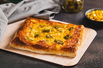 Spicy pizza with jalapeno pepper, corn and cheese on a wooden board