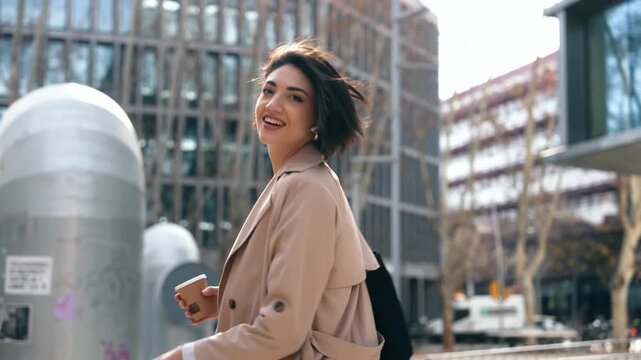 Businesswoman strolls city, turns around smiling with coffee in hand