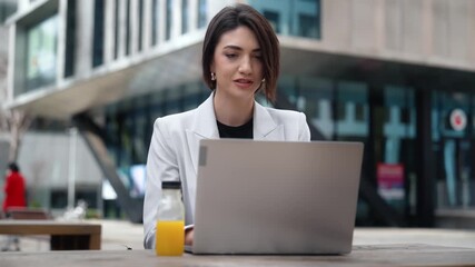 Businesswoman smiles while working on her laptop outdoors - Powered by Adobe