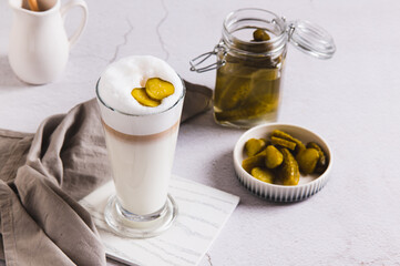 Picklatte with foam in a glass and pickles in a bowl on the table