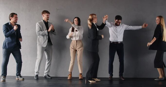 Slow motion video of group of joyful excited young business people men and women having fun in office. Company employees celebrating success dancing indoors. Success and teamwork concept. 4k video.