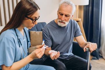 Female doctor, nurse checking blood glucose level for senior man at home
