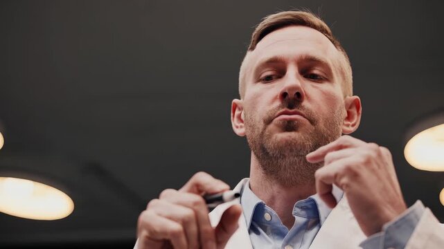 Doctor examining with penlight lamp. Male clinician in labcoat performs medical examination. Healthcare pro inspects under ceiling lighting. Serious pro looks down. Ceiling lights highlight subject.
