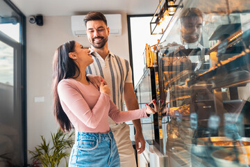 Happy young couple in bakery paying for pastries using smartphone.