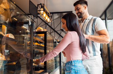 Happy young couple in bakery paying for pastries using smartphone.