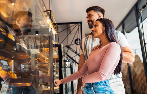 Happy young couple in bakery paying for pastries using smartphone.