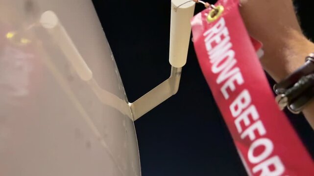 Closeup view of the hand of a white pilot wearing bracelets placing the pitot cover cap with the Remove Before Flight legend after the last night flight.
