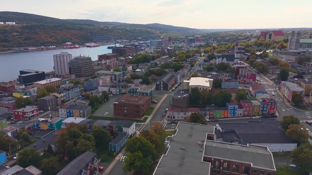 A panoramic aerial over St. John's Newfoundland in autumn captures the harbour shimmering at dusk, colourful city streets climbing the hillside, and calm waters reflecting the soft evening light.