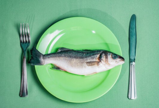 Raw fish on green plate with cutlery in restaurant still life