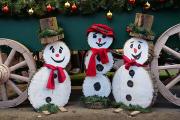 Three cheerful wooden snowmen are smiling. Snowmen are wearing hats and scarf