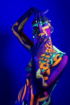 Artistic portrait of woman with colorful body paint under UV light in studio
