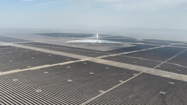Aerial view of a vast solar power plant with a central tower surrounded by mirrors reflecting sunlight, creating a bright and futuristic landscape, Turpan, China.