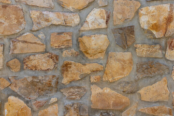 Irregularly shaped natural stones in warm earth tones forming a rustic patterned wall, showcasing robust texture and an authentic, durable architectural backdrop for various uses