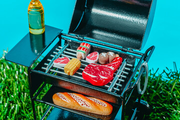 Toy barbecue grill with meat corn bread and beer outdoors in summer