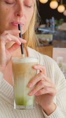 Woman enjoying iced matcha latte in cozy cafe wearing white sweater and relaxing alone