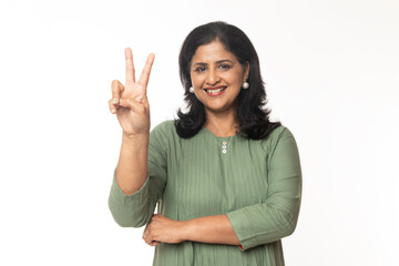 Portrait of Indian woman raising two finger to show the count of two, standing against white background.