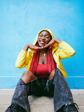Young woman with braids in yellow jacket smiling playfully outdoors