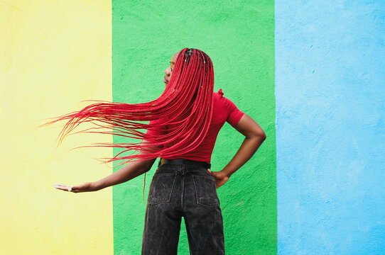 Woman with red braids posing playfully against colorful wall outdoors