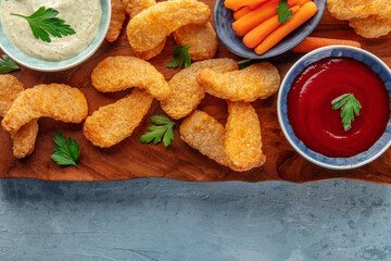 Chicken nuggets with fresh vegetables and dips, on a wooden board, shot from the top with coy space