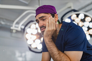 A surgeon in scrubs looks stressed in an operating room, possibly after a difficult procedure.