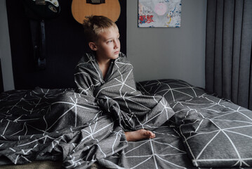 A handsome blond boy is lying in bed