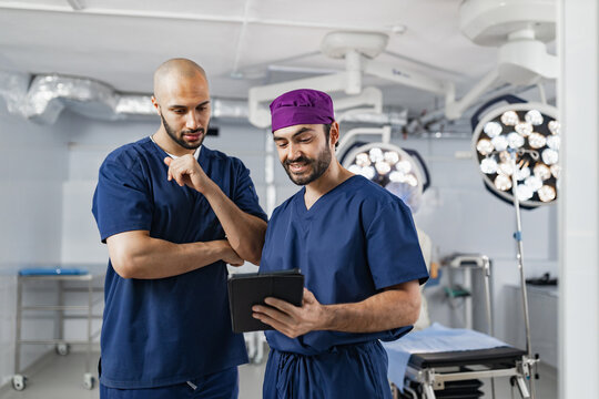 Two surgeons in scrubs review a tablet in an operating room, discussing a procedure with focused expressions.