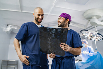 Two surgeons examine an X-ray scan in an operating room, with another medical professional in the background.