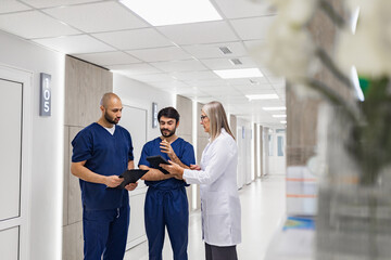 A doctor and two medical staff members are discussing in a clinic hallway, reviewing medical...