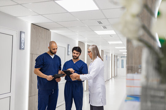 A doctor and nurses review medical records in a clinic hallway, discussing patient care and treatment plans.