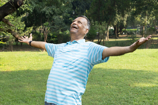 Indian happy senior man spreading hands at park. Wearing blue strip half sleeve color t-shirt. Concept of successful, confident healthy senior and wellness, elder enjoying after after retirement