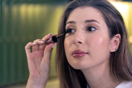 Young woman applying mascara by mirror. Close beauty moment.
