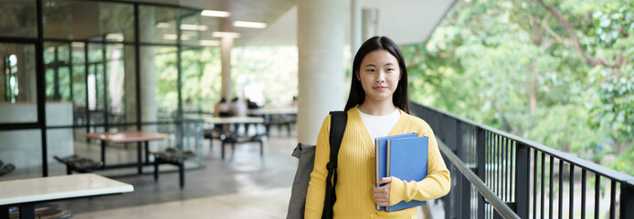 student girl holding books and carry school bag while walking in school campus background, copy space banner, education, back to school concept