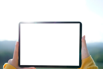 Woman hand holding a tablet with blank white screen with copy space. In the background blurred lake and sky. Remote work lifestyle and creative thinking in nature concept.