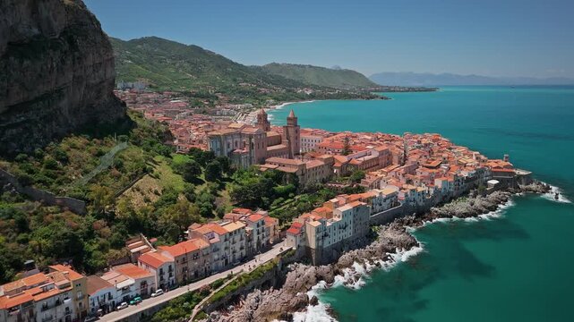 Aerial view of Cefalu Old Town on a coastal headland with the Cathedral and terracotta rooftops along the Tyrrhenian Sea, sunny day, Sicily, Italy