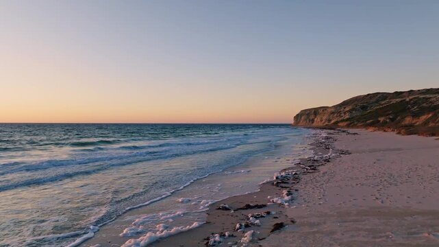 Aerial view of the sun kissed beach with gentle waves reaching the shore, next to a cliff, Port Willunga, South Australia, Australia.