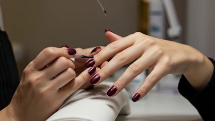 Professional manicure in progress applying dark red nail polish