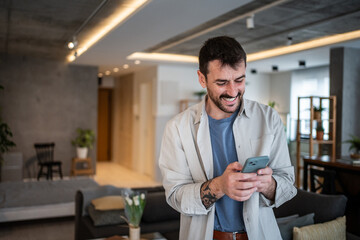 Fototapeta premium Young man smiling, using smartphone connecting social media