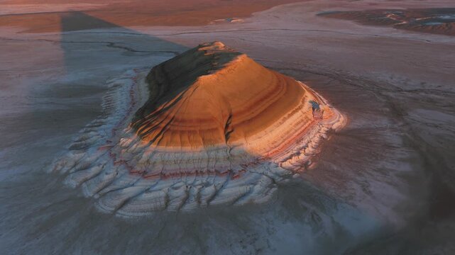 Aerial view of the majestic Mount Bokty shows the landscape bathed in warm light, contrasting with the cool tones of the surrounding terrain, Mount Bokty, Mangystau Region, Kazakhstan.
