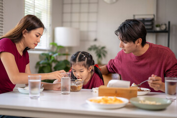 Asian family having dinner, parents feeding daughter