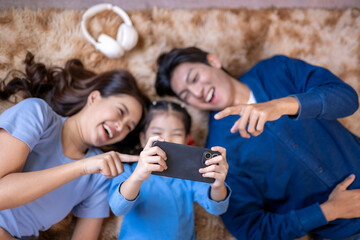 Asian family laughing, laying on floor, watching smartphone screen